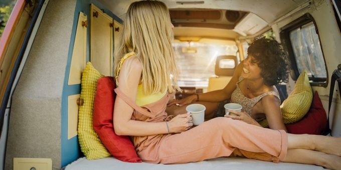 Deux femmes assises sur un matelas dans un van en buvant le café.