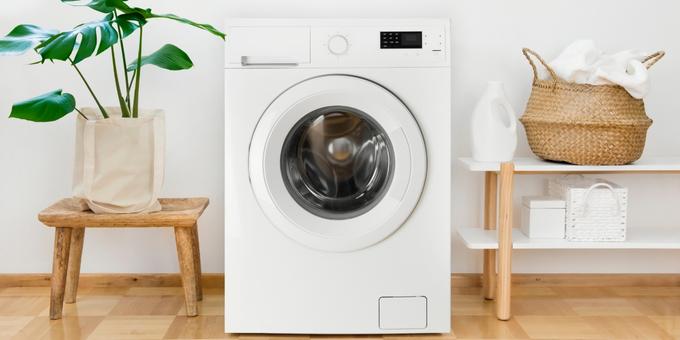 Machine à laver vide avec un meuble à droite et une plante à gauche.